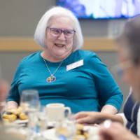 Sandy Allen smiling while listening to someone at his table